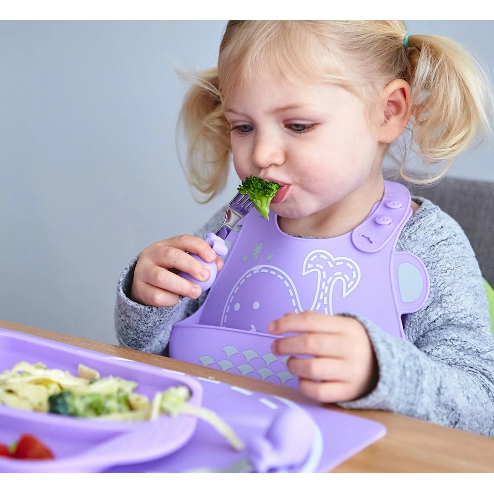 Marcus & Marcus Palm Grasp Fork And Spoon with purple handles, toddler eats broccoli using the easy-grip utensils.
