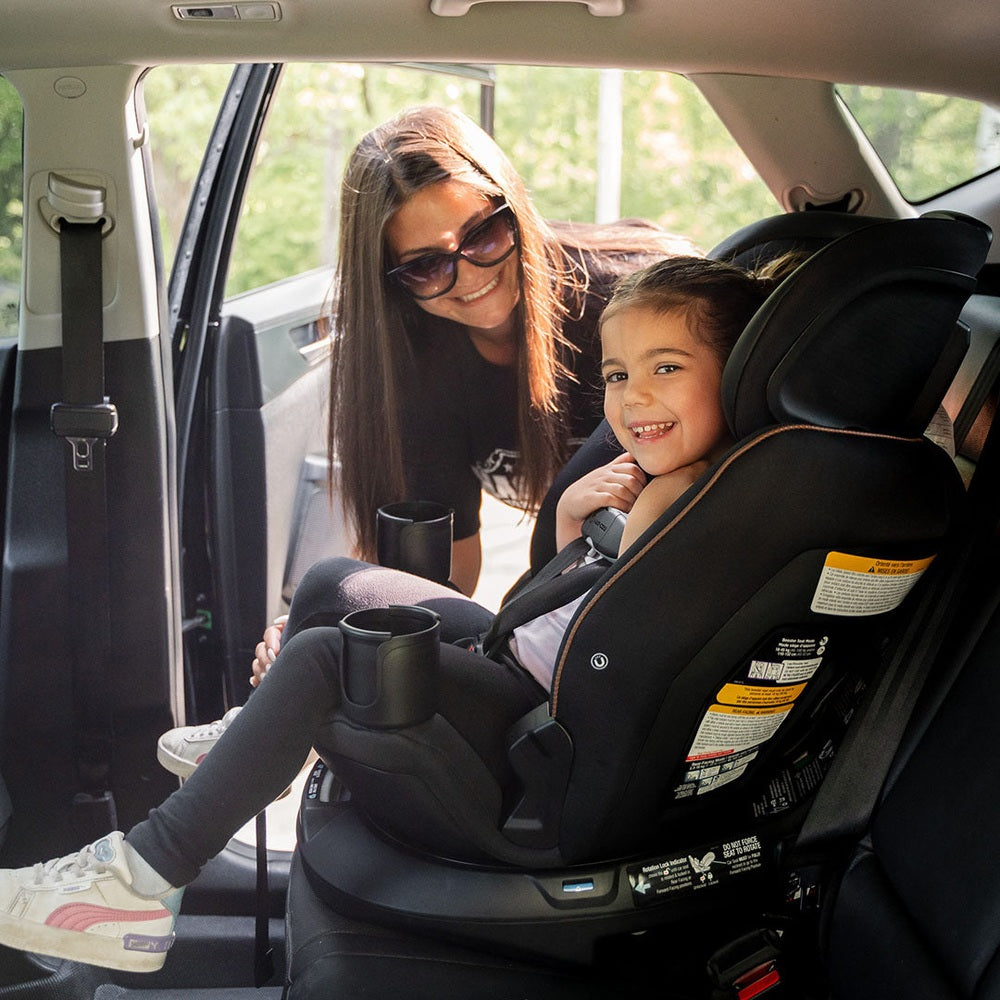 MAXI COSI Andi 360 rotating all-in-one convertible car seat in black upholstery installed in car with smiling child.