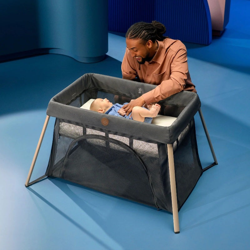Maxi-Cosi Calao travel crib in dark gray with mesh sides; father interacting with baby.