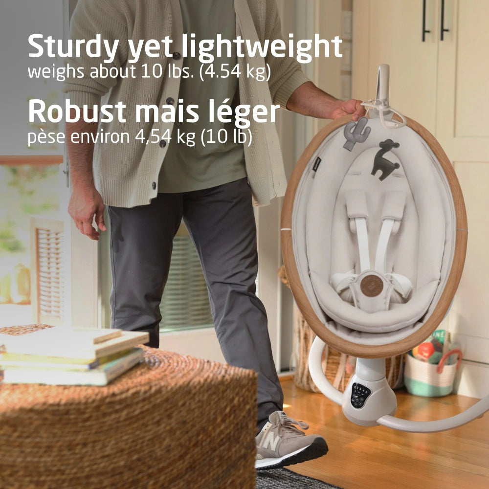 Maxi Cosi Cassia Swing, lightweight beige baby swing with wooden ring and gray padded seat, shown being carried by an adult.