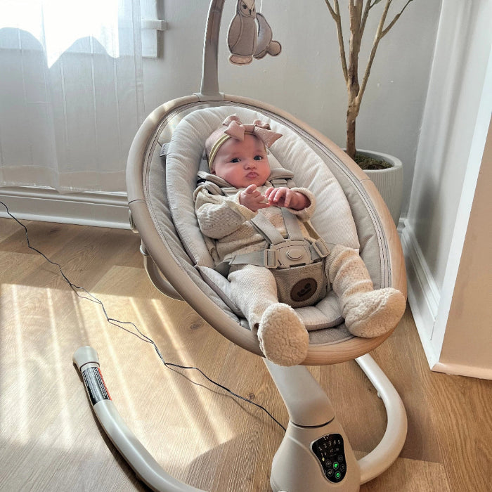 MAXI COSI Cassia Swing in cream; cushioned seat with safety harness, baby gently nestled in swing.