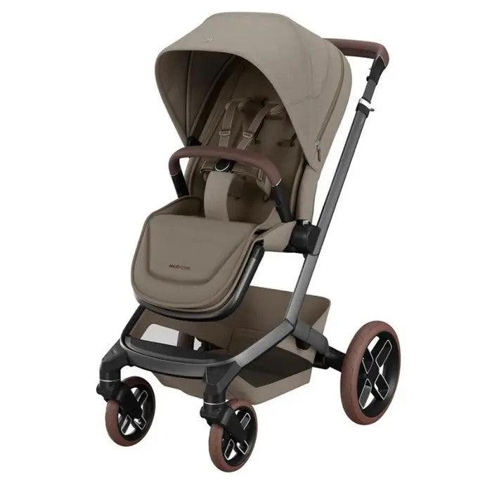 Maxi Cosi Fame stroller in beige fabric with canopy raised, brown handles, and a storage basket while rolled on four wheels.