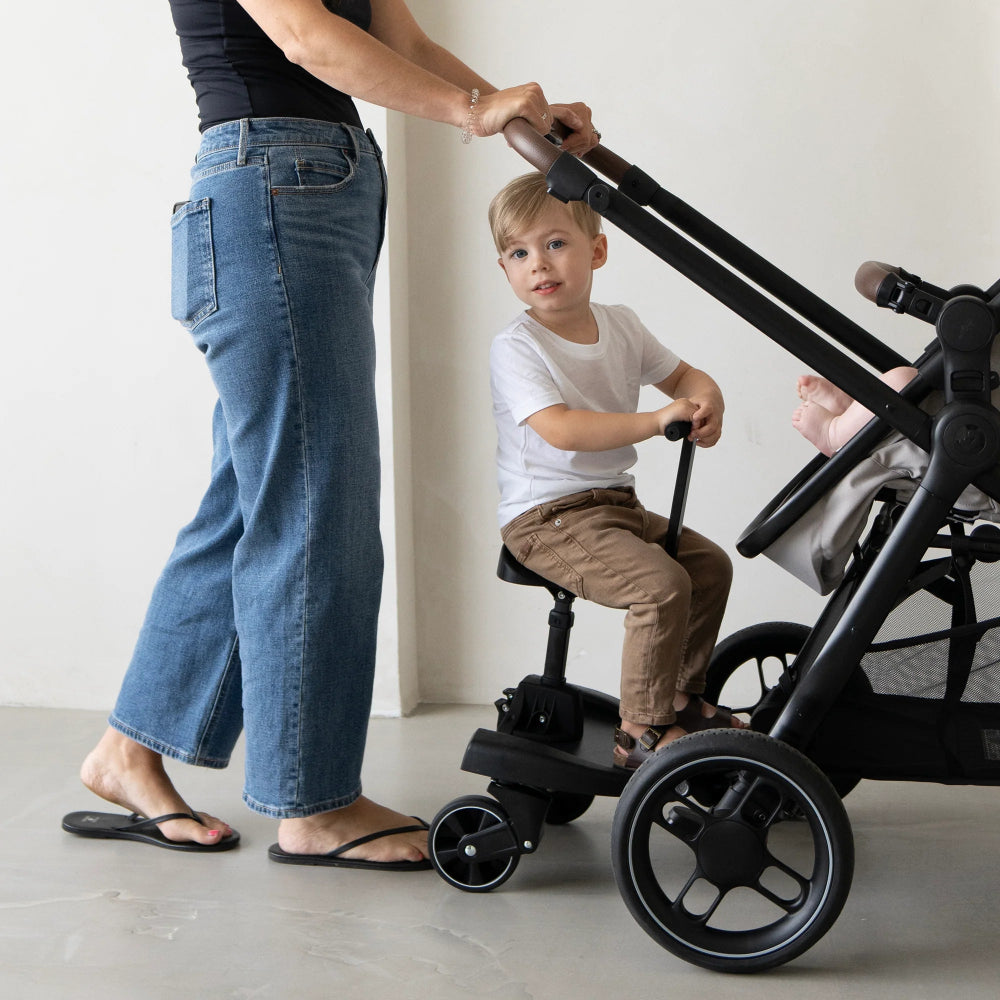Maxi-Cosi Hop-On Board for strollers; toddler seated on the board behind the stroller, black frame.