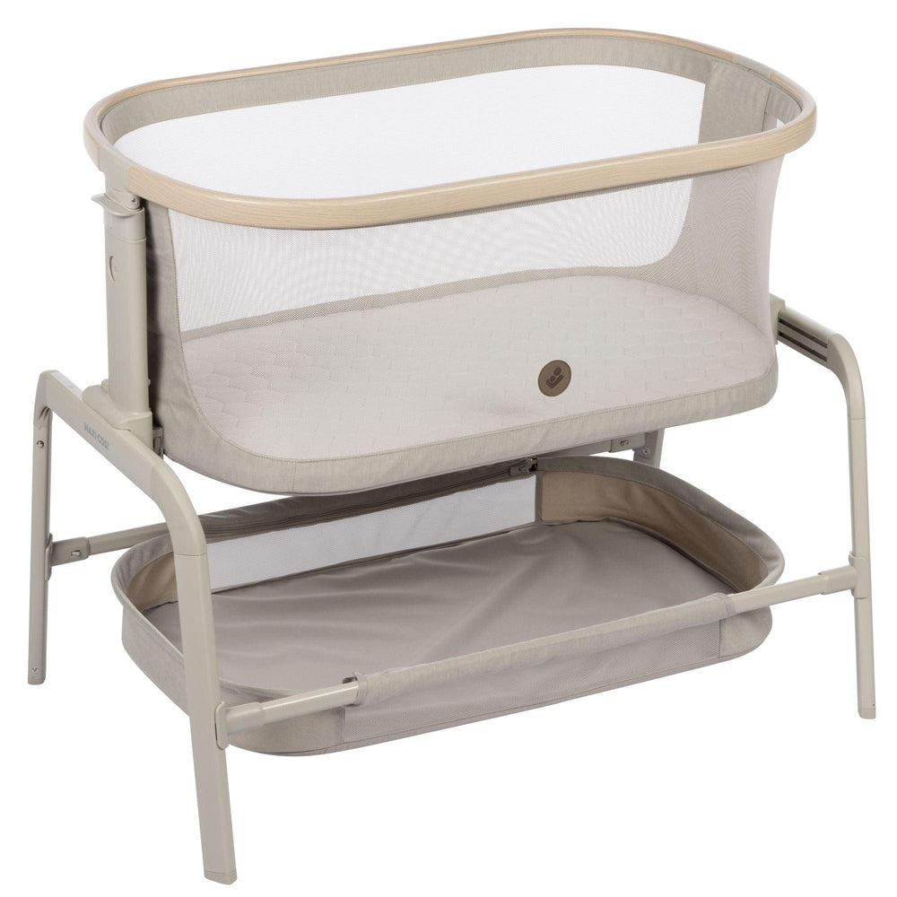 MAXI COSI Iora bedside bassinet in beige with mesh sides, on a sturdy frame and lower storage shelf.