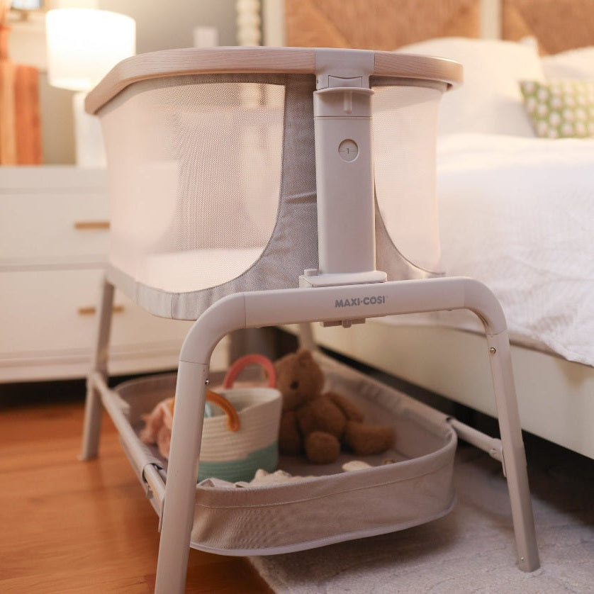 MAXI-COSI Iora bedside bassinet in soft grey with mesh sides on a light wood frame