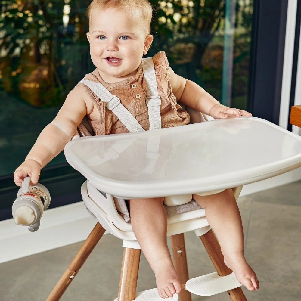 Maxi Cosi Moa 8-in-1 high chair with white tray and wooden legs; baby in brown outfit