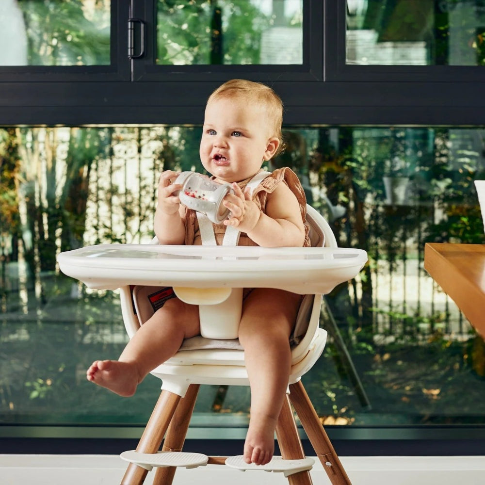MAXI COSI Moa 8-in-1 high chair in white with wooden legs, baby seated in tray