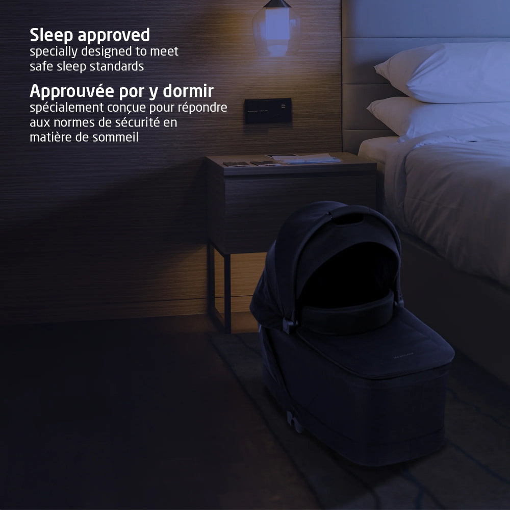 Maxi-Cosi Oria2 Carrycot Twillic Black in dark twill fabric placed beside a bed in a modern bedroom