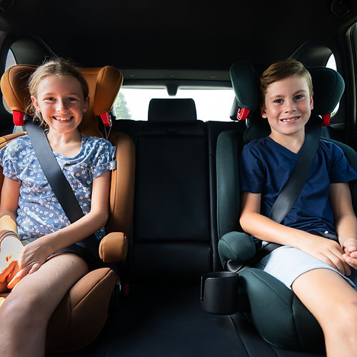 Maxi-Cosi Rodisport Booster Car Seat: two kids buckled in orange and green boosters, demonstrating secure seat belts.
