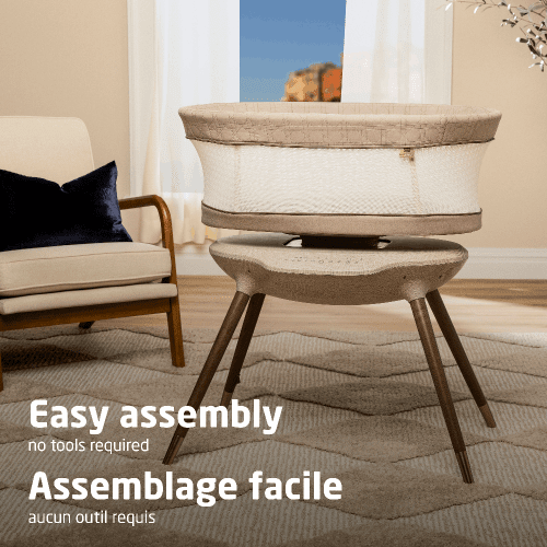 Maxi Cosi Starling Smart Bassinet on a wooden stand with beige fabric in a cozy living room.