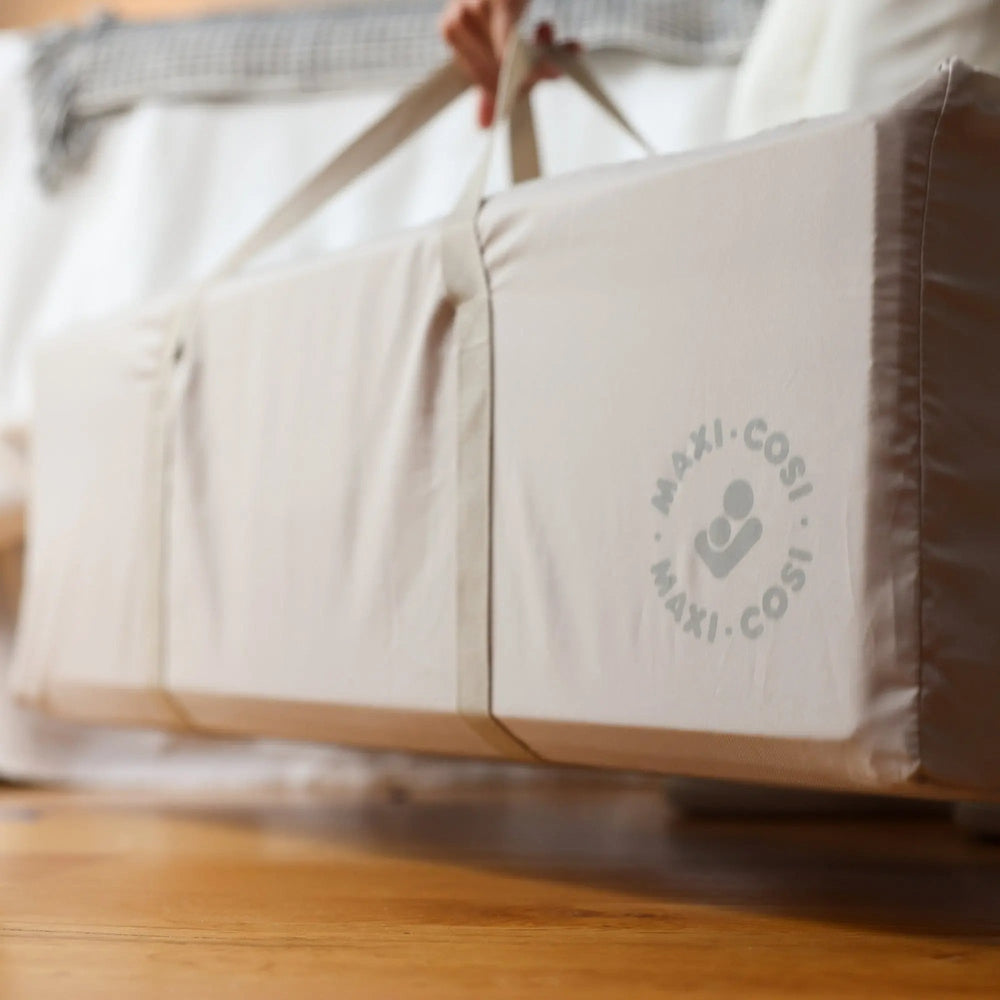 MAXI-COSI Swift Playard in cream fabric with carrying straps, showing portable bassinet and playard.