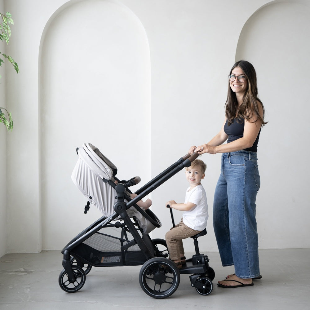MAXI COSI Zelia Luxe 5-in-1 modular travel system stroller in gray, mom pushing with toddler seated.