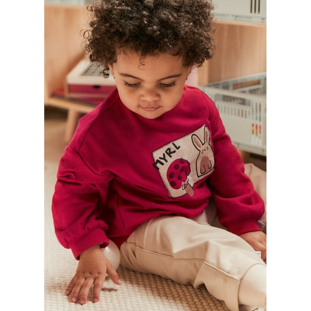 Mayoral Baby Pants and Sweater Set Red: toddler girl in red knit top with patch, beige pants, sitting on rug.