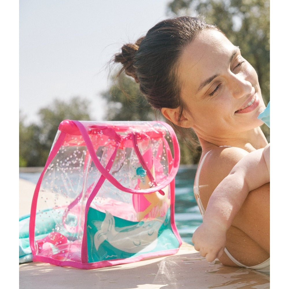 Mayoral Baby Transparent Beach Backpack in pink PVC with clear panels showing dolphins, held poolside by a smiling woman.