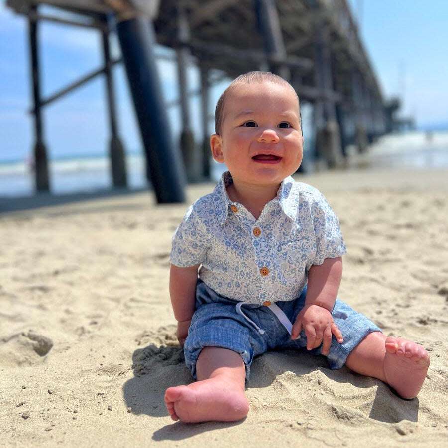 Me & Henry Helford blue floral woven onesie worn by a baby on a sandy beach