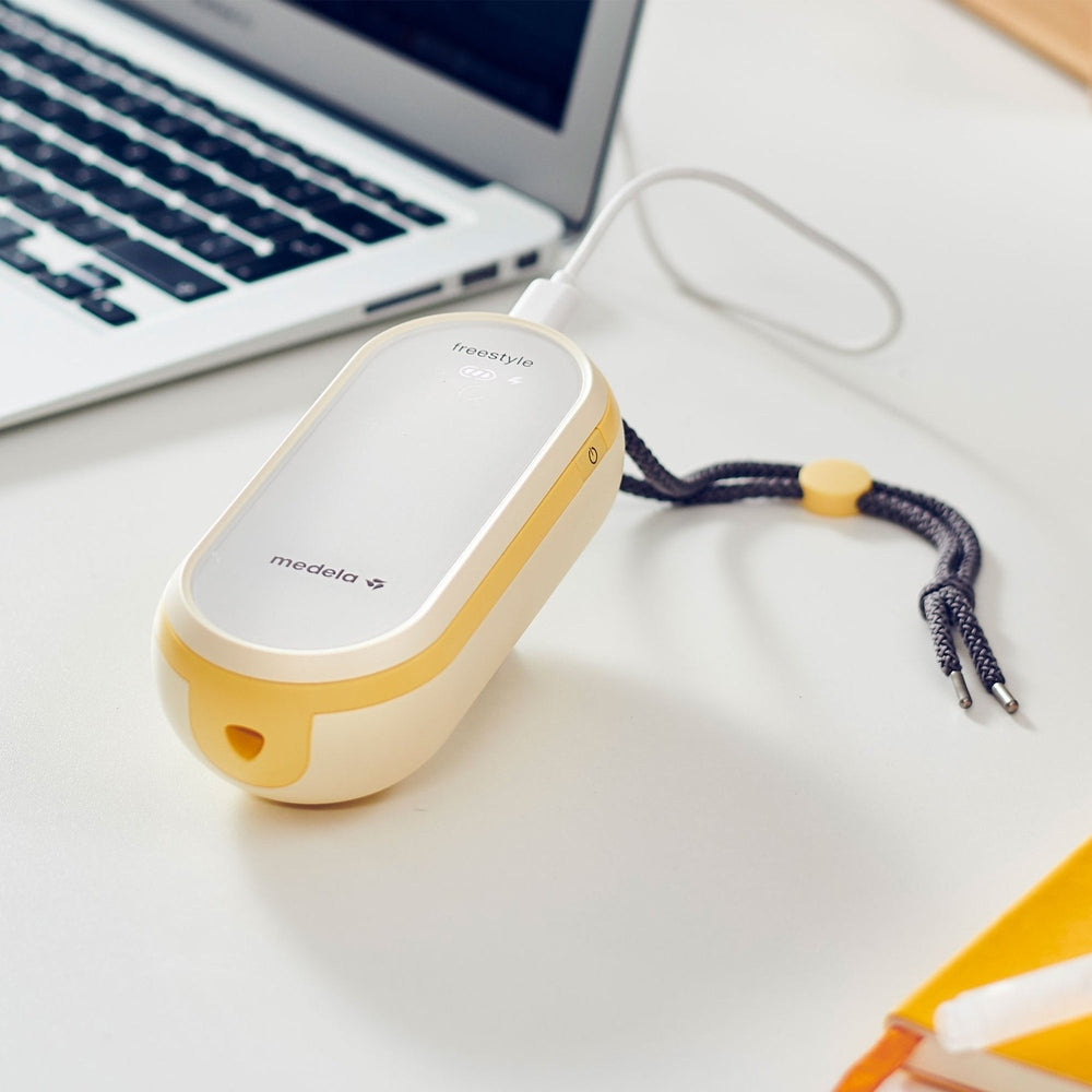 Medela Freestyle Flex breast pump, double electric in yellow and white on a desk beside a laptop
