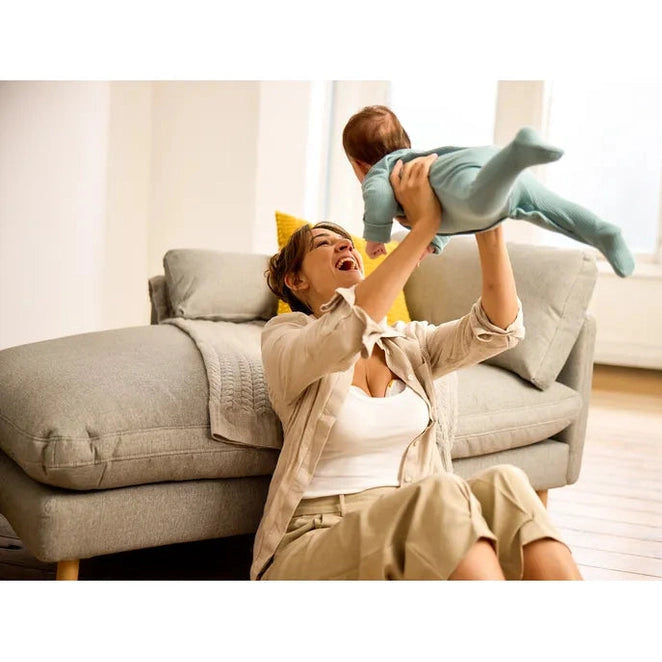 Medela Magic InBra Wearable Breast Pump: joyful mom lifts baby overhead on sofa, demonstrating hands-free comfort.