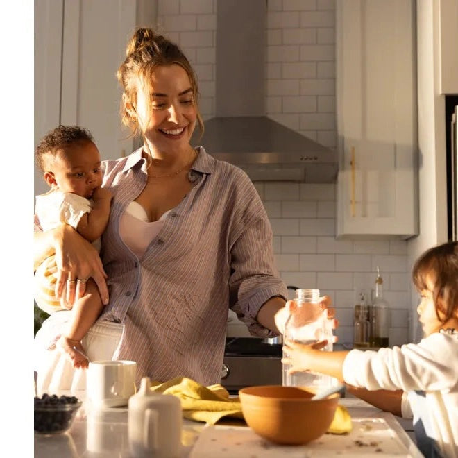 Medela Motion Inbra Double Electric Breast Pump; mom in a bright kitchen pumps while cradling her baby.