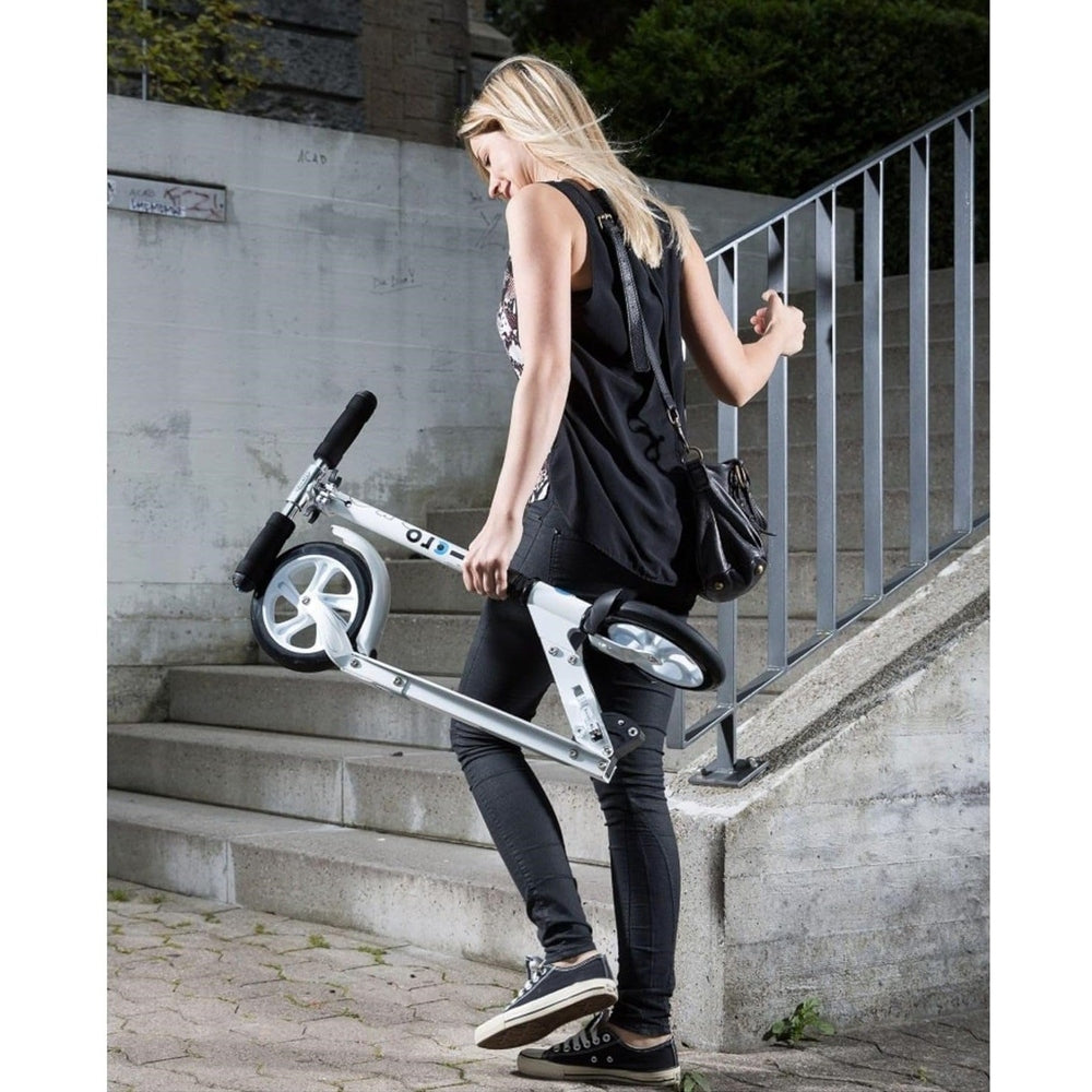 Micro Classic White Scooter, folded and portable with a silver frame and black grips, carried by a woman in black.