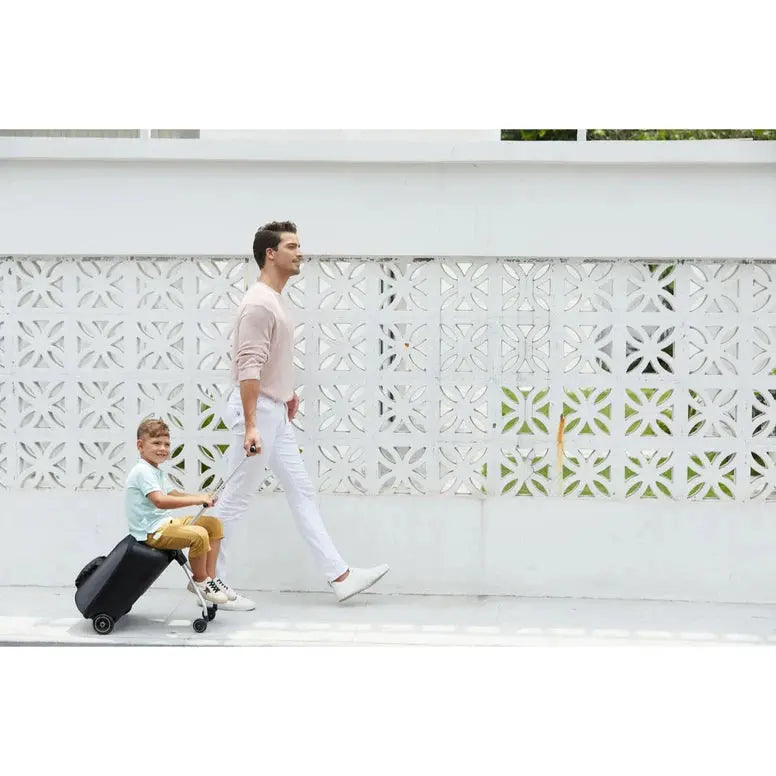 Micro Eazy Luggage black wheeled suitcase; a child sits on it while an adult walks beside.