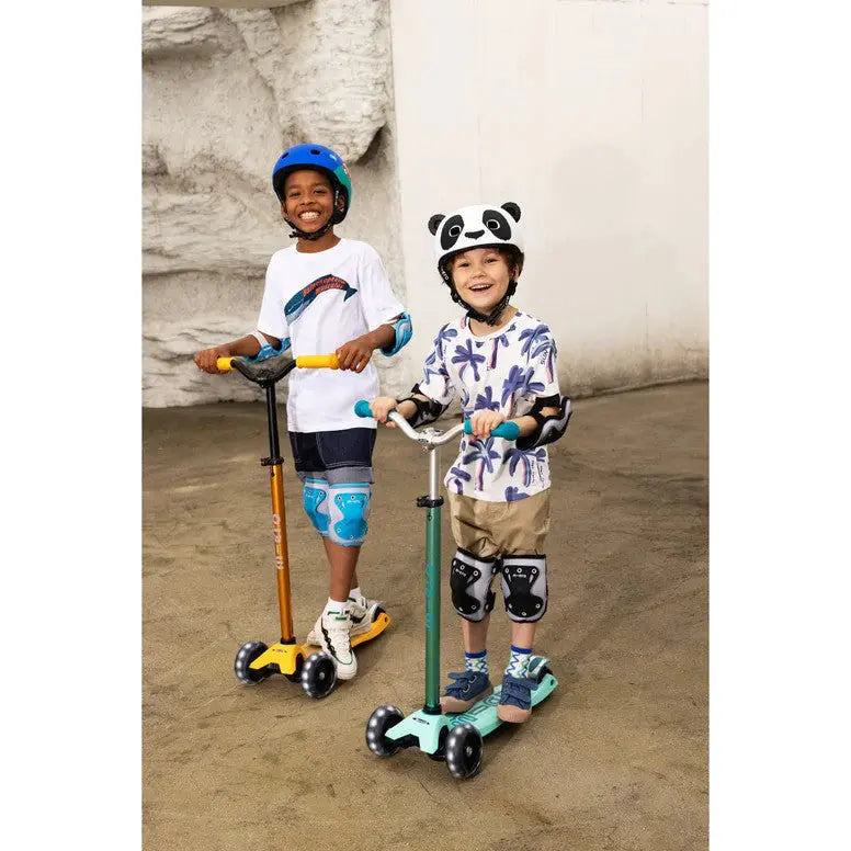 Micro Helmet V2 Panda: two kids ride teal and orange scooters, wearing panda helmets and knee pads.