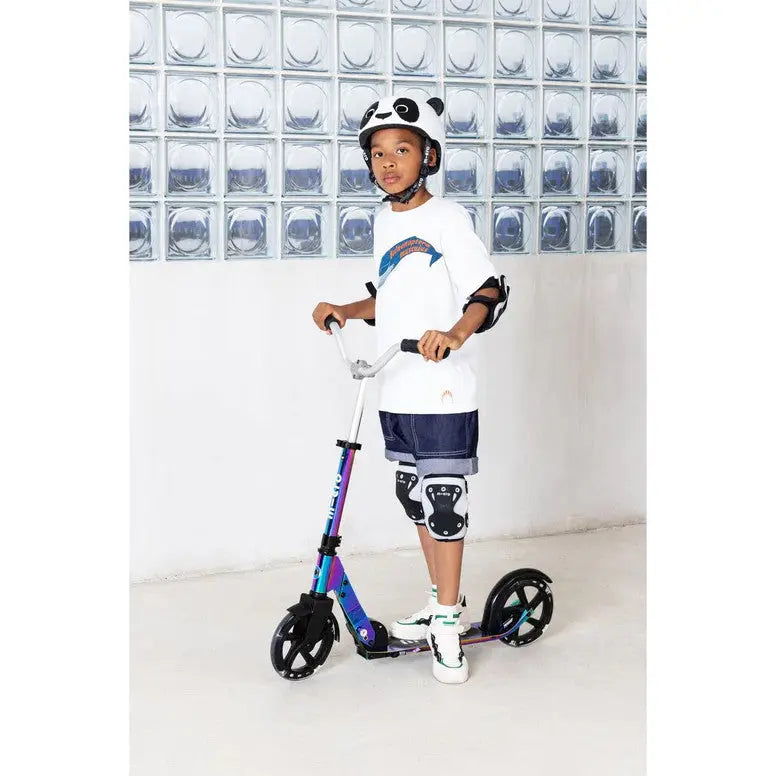 Micro Helmet V2 Panda kid wearing panda helmet and knee pads while riding a colorful kick scooter.