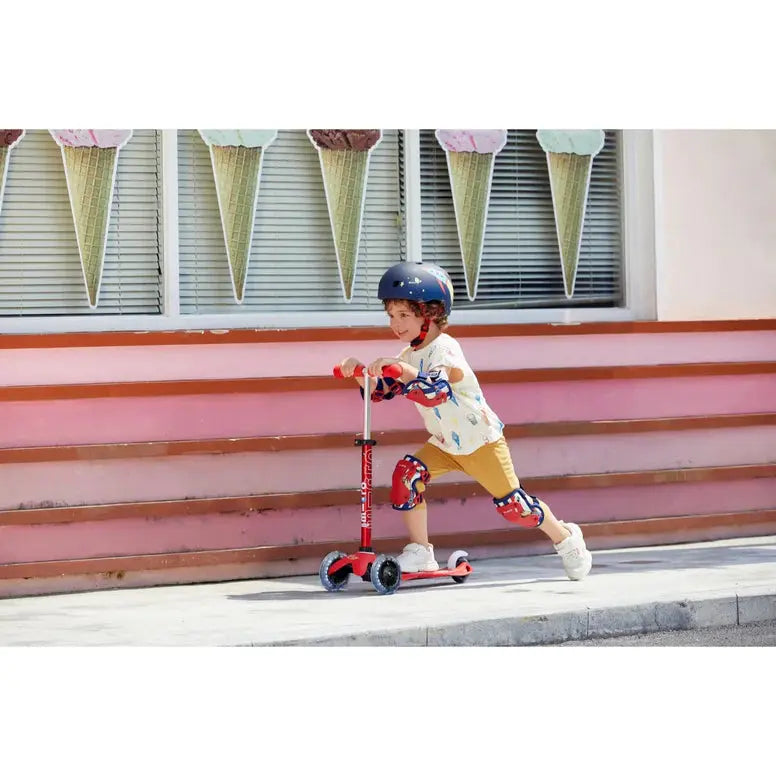 Micro Helmet V2 Rocket worn by a child riding a red Micro scooter, with knee and elbow pads for protection.