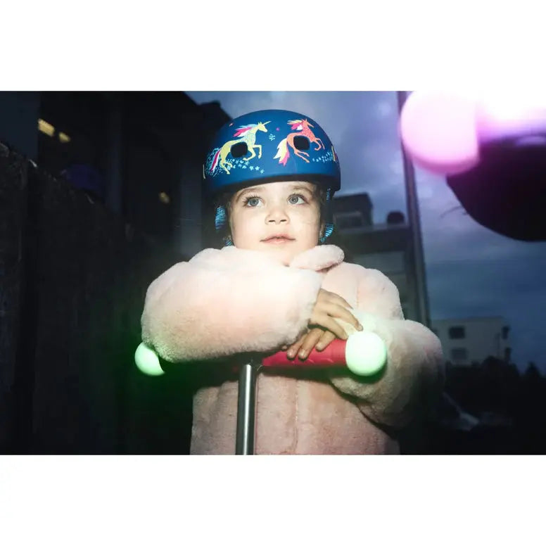 Micro Helmet V2 Unicorn blue helmet with unicorn graphics worn by a child riding a scooter with glowing green handlebars