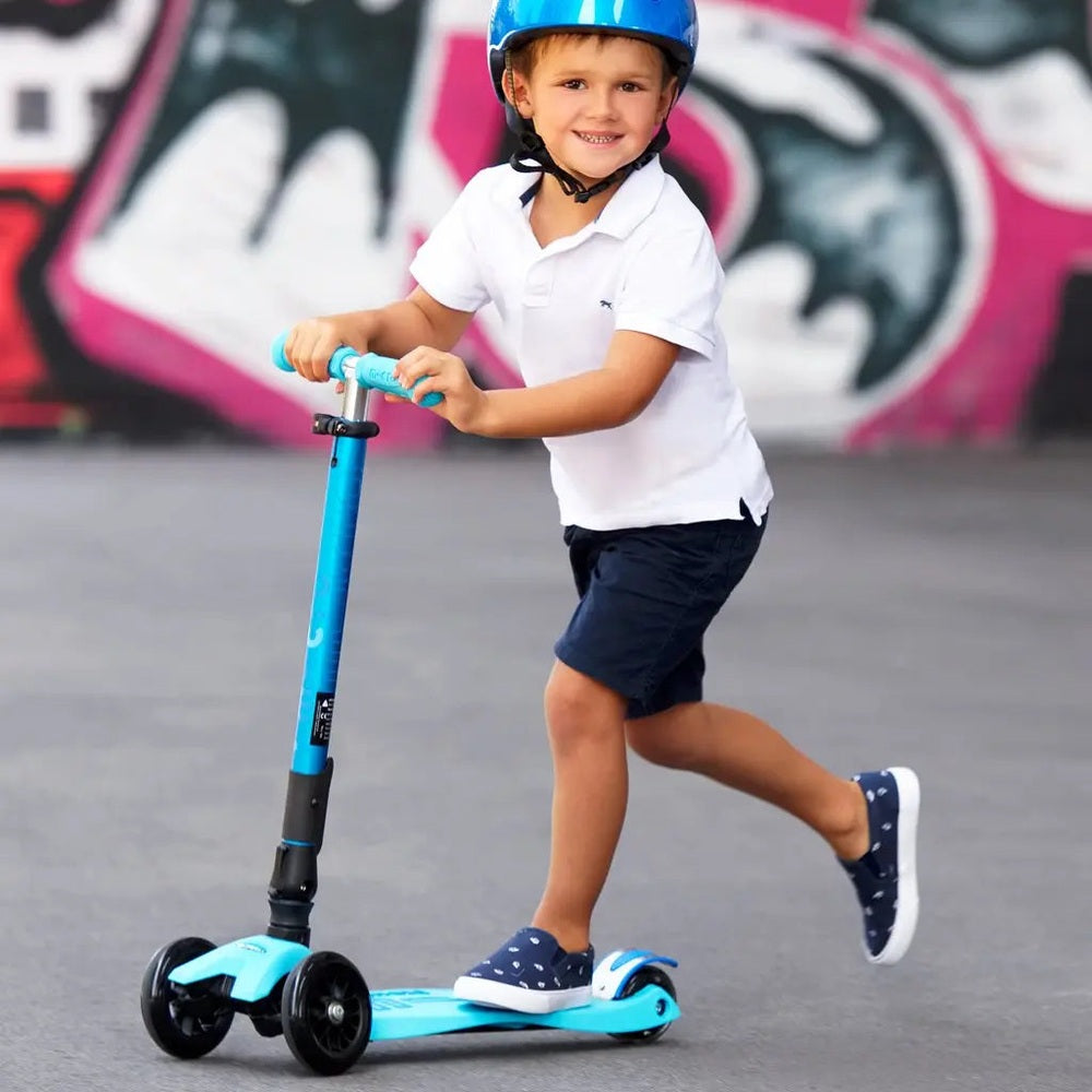 Micro Maxi Foldable Deluxe LED Scooter; blue frame with black wheels as a child rides outdoors in a helmet.