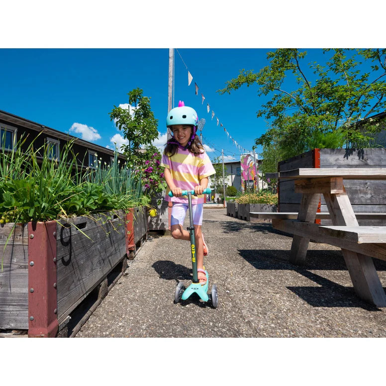 Micro Mini Deluxe Eco Scooter Green for kids, turquoise helmet worn on sunny outdoor path.
