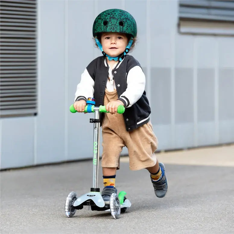 Micro Mini Deluxe Flux LED scooter for kids with green handlebars, child wearing a green helmet.
