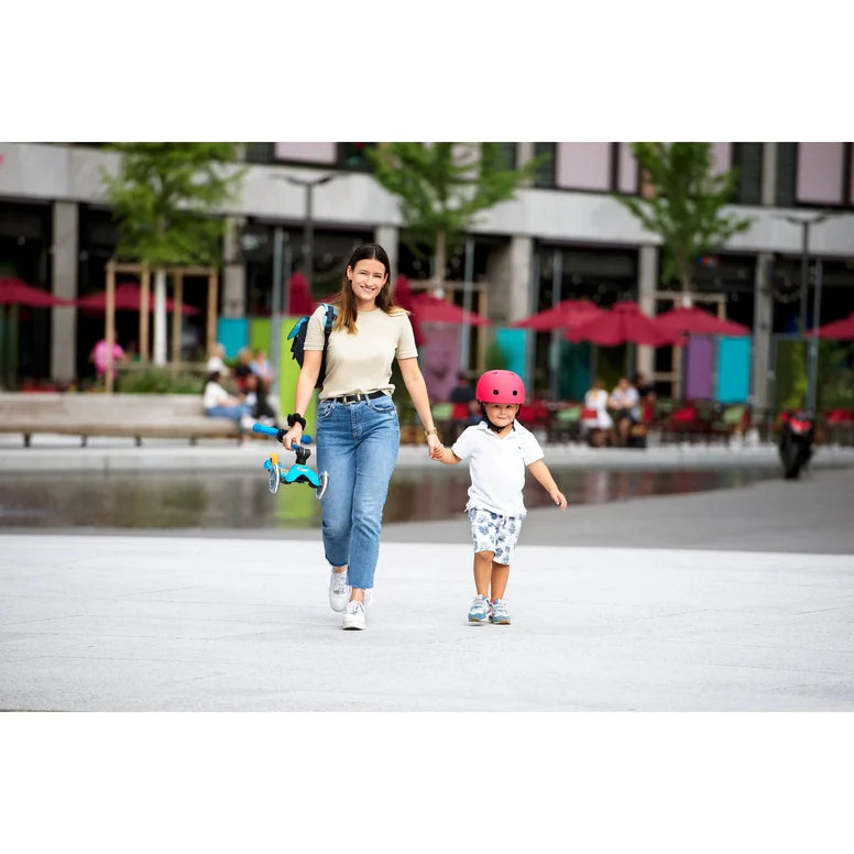 Micro Mini Deluxe Foldable LED Scooter with blue accents carried by a woman walking with a child in a city plaza.