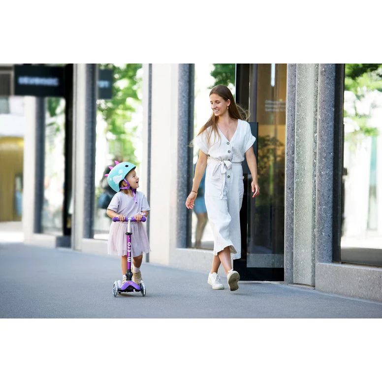 Micro Mini Deluxe Foldable LED Scooter for kids; helmeted child rides the purple scooter beside a smiling woman.