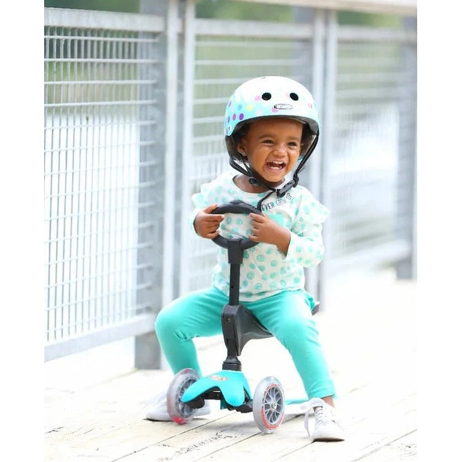 Micro Mini Seat With O-Bar riding toy in teal frame; child steers and smiles while wearing a helmet.