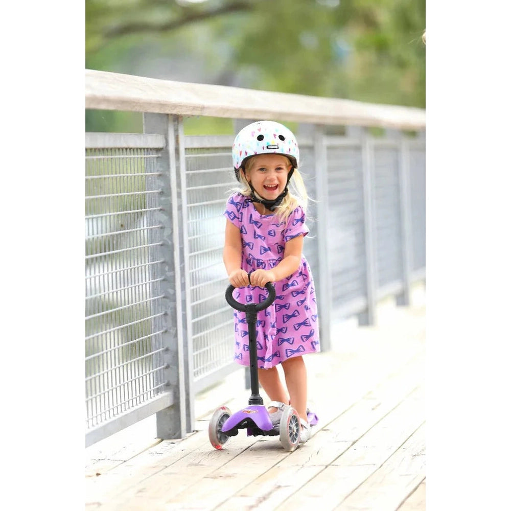 Micro Mini Seat With O-Bar riding toy, purple scooter, girl in helmet smiling on boardwalk.