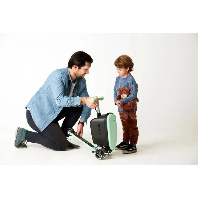 Micro Scooter Junior Luggage Mint carry-on suitcase with built-in scooter; father kneeling to help child with the mint scooter.