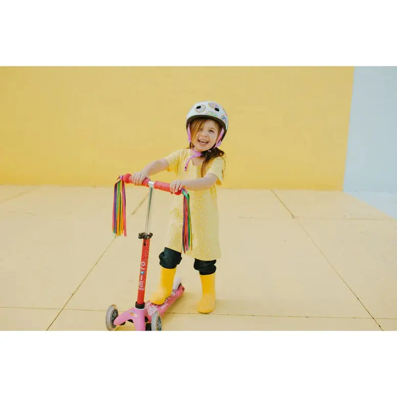Micro Scooter Streamers: pink scooter with rainbow handlebar streamers, worn by a smiling girl in yellow riding outdoors