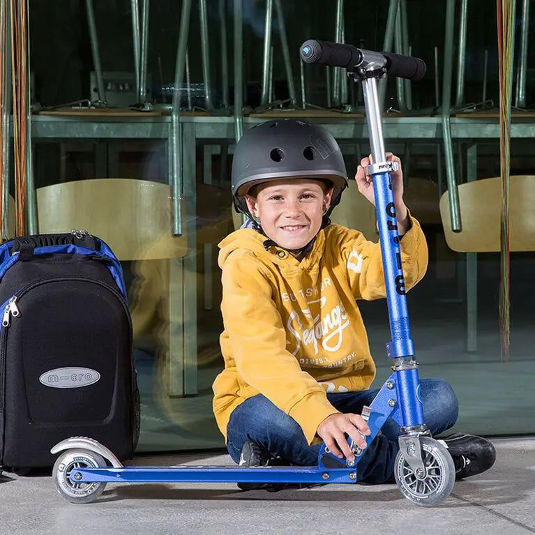 Micro Sprite Scooter being ridden by a smiling child in a yellow hoodie, showcasing its blue aluminum frame and grey wheels.