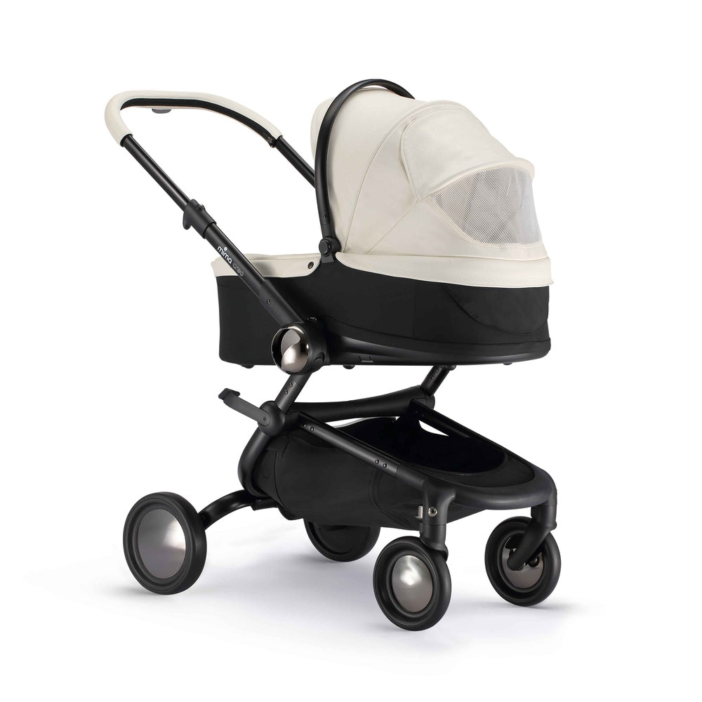 Lifestyle image of a white Mima Creo bassinet on stroller frame outside a café.