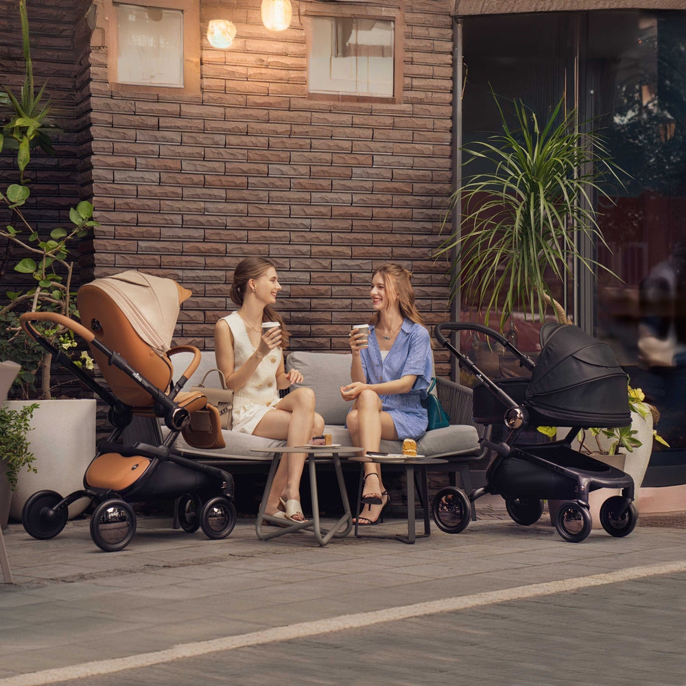 Lifestyle image of the Mima Creo stroller with black bassinet and mocha cream stroller at an outdoor café.