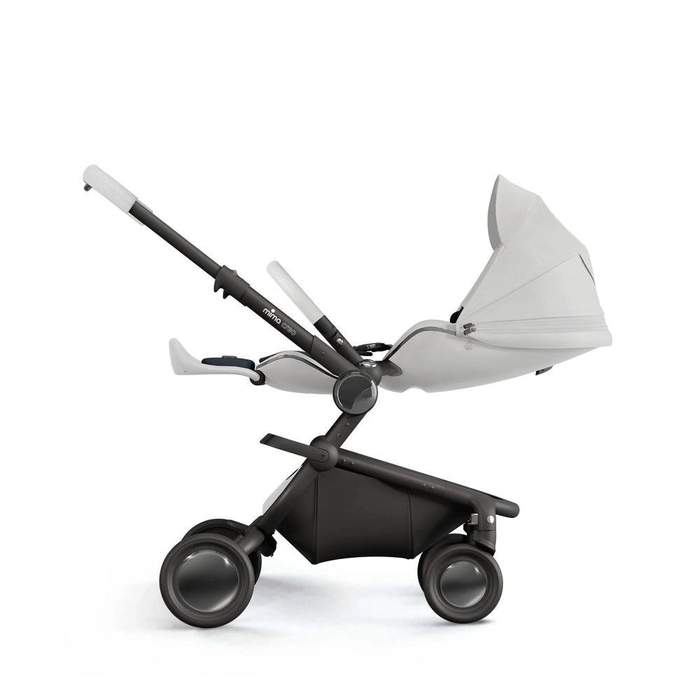Mima Creo Stroller with white bassinet on a sleek black frame, being wheeled by the handlebar.