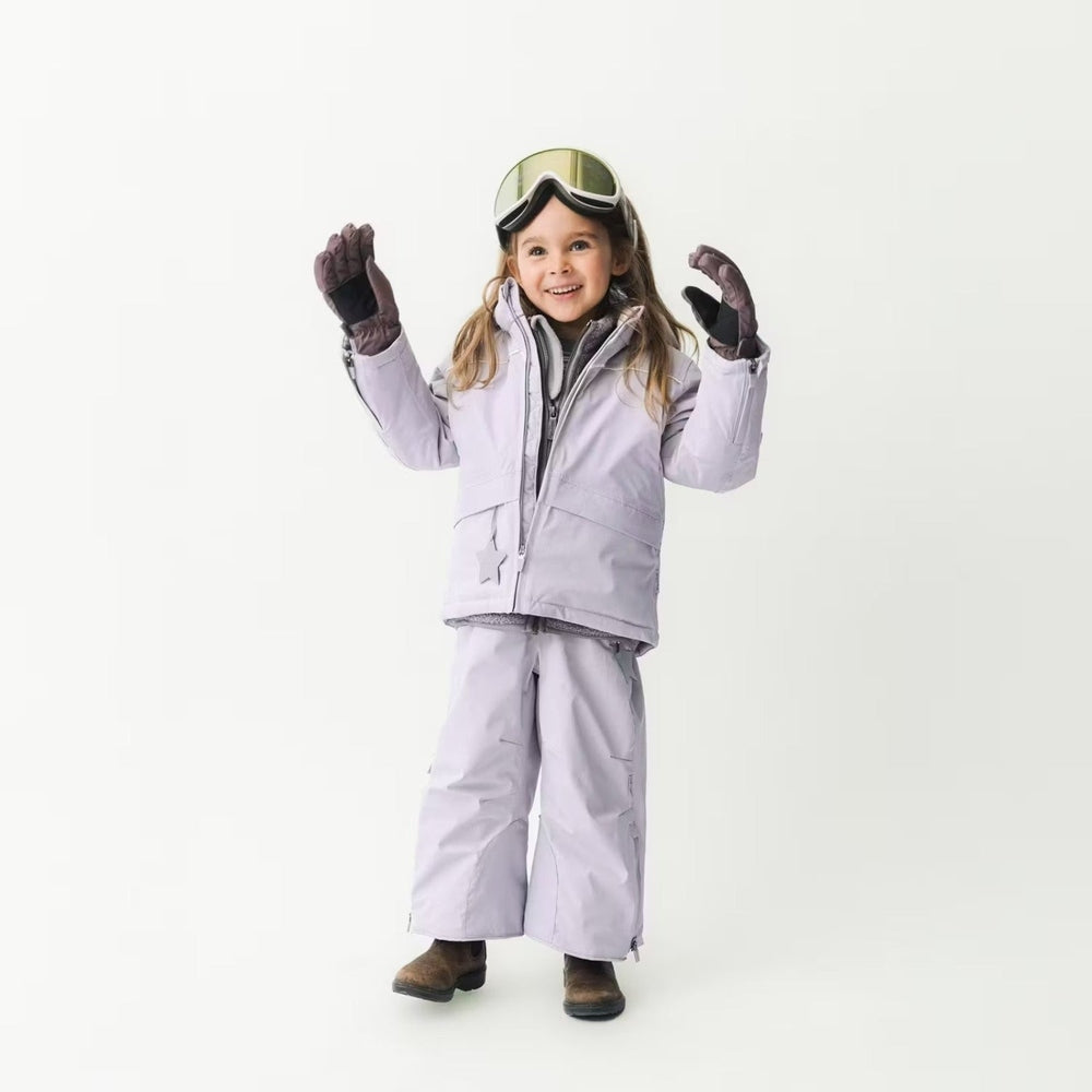 MINI A TURE Matadane Ski Tech Jacket Grs Purple Raindrops worn by a smiling girl in lavender ski suit, lifting gloved hands.
