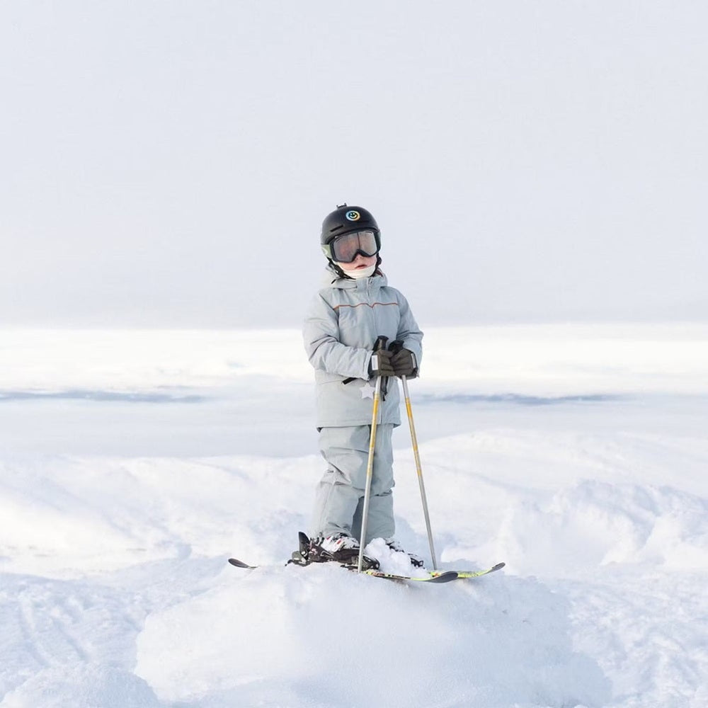 MINI A TURE Matadane Ski Tech Jacket Grs Quarry worn by a child on skis, helmeted and gripping poles in fresh snow.
