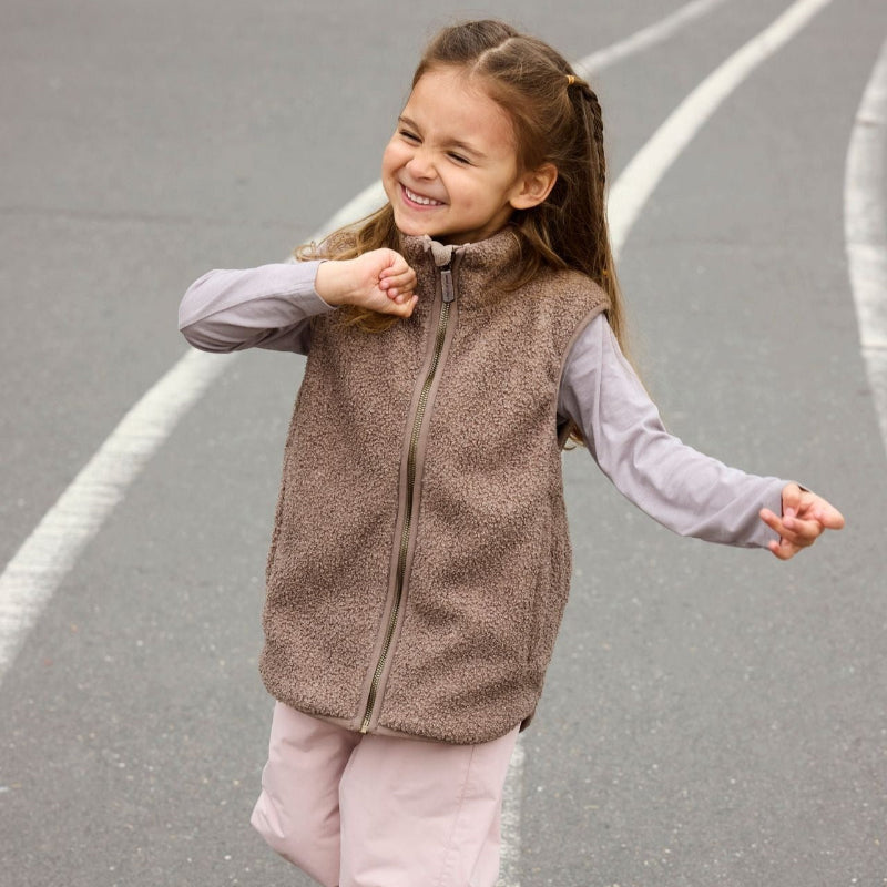 Mini A Ture Matbattal teddyfleece vest in brown, worn by a smiling toddler in a lavender top