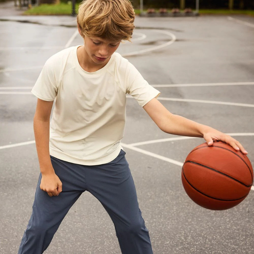 Mini A Ture Matbjergi T-Shirt Grs Papyrus White worn by a boy dribbling a basketball on an outdoor court.