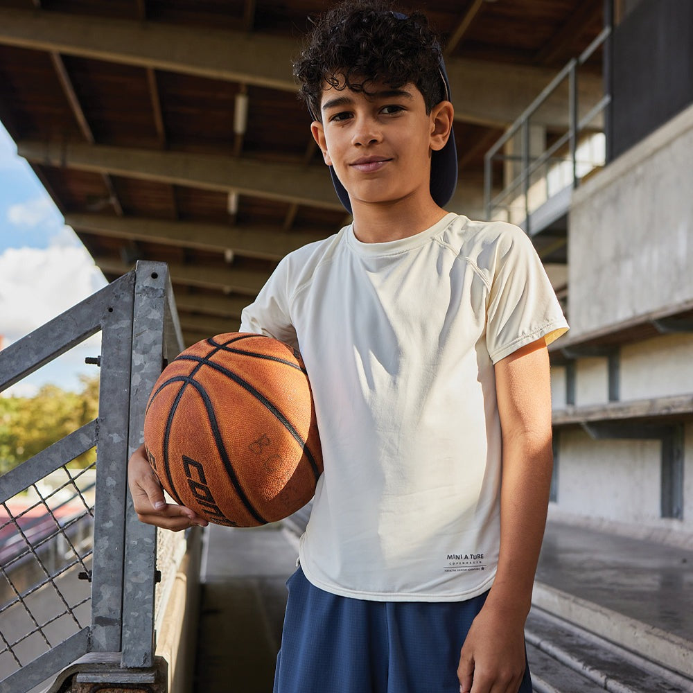 Mini A Ture Matbjergi T-Shirt Grs Papyrus White worn by a boy on an outdoor court, white short-sleeve top