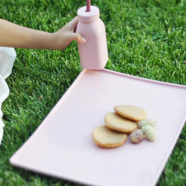 Minikoioioi Bottle & Straw pink held by a child over a pink tray outdoors, showing the attached straw.