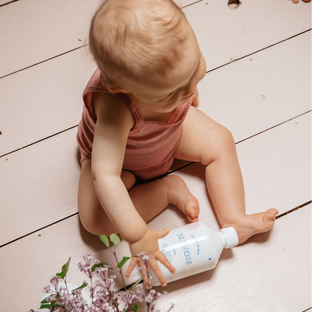 Minois Paris Bath Foam 500 ml bottle, white plastic with blue lettering, baby playing on floor