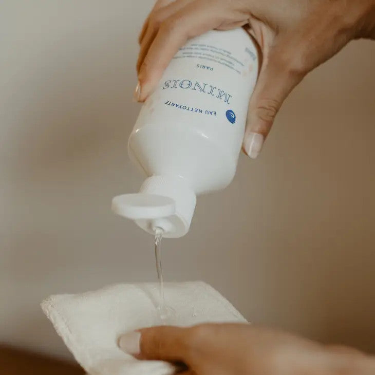 Minois Paris Cleansing Water 250 ml pouring onto a cotton pad for baby skincare