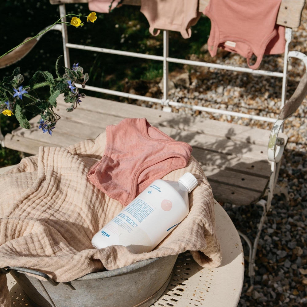Minois Paris Kerzon fragranced laundry soap bottle in a metal tub with beige towel and pink baby onesie